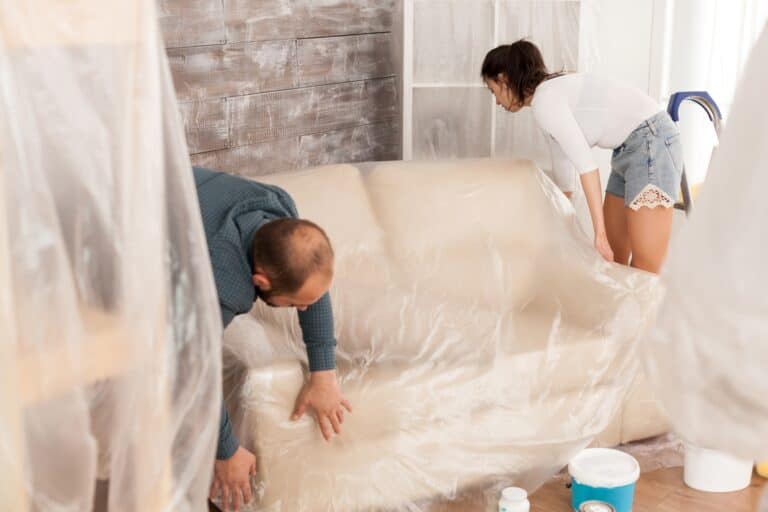 A couple is wrapping a sofa with plastic